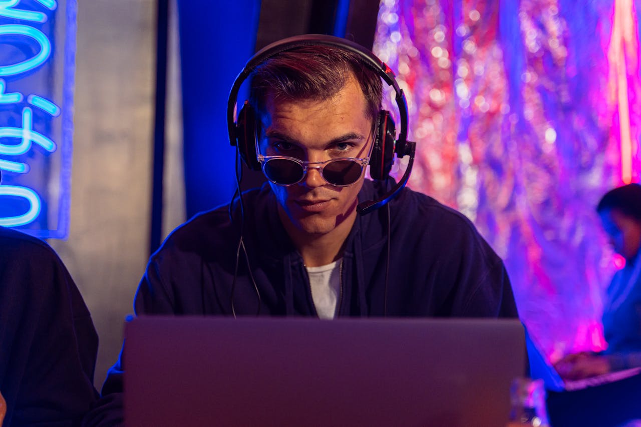 digital Focused man in headphones and sunglasses uses laptop in vibrant studio setting.